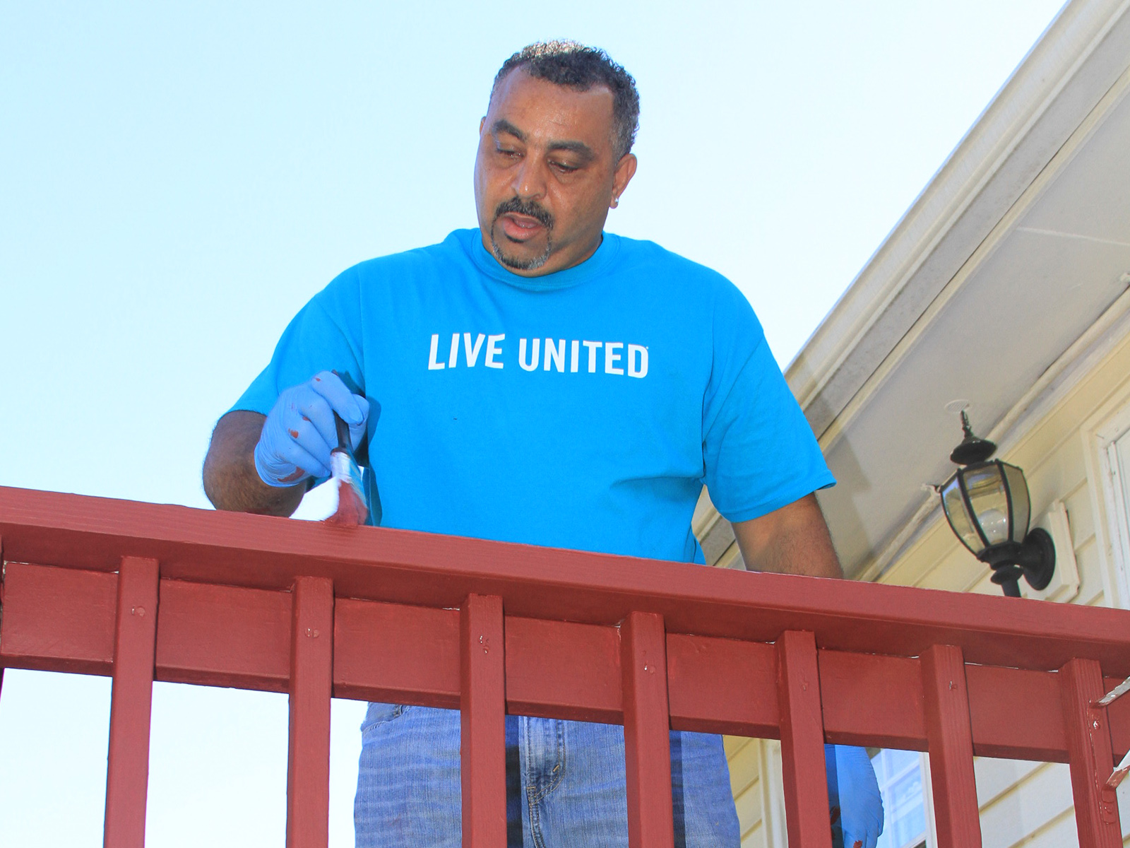 Volunteer in Live United tee shirt painting a railing