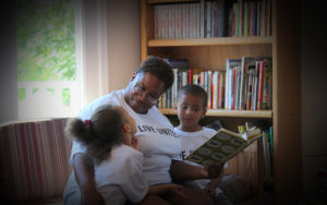 Photo of mother and two children wearing "Live United" tee-shirts, smiling, reading together.
