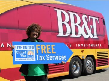 photograph of volunteer holding Free Tax Services sign in front of B B and T tax bus
